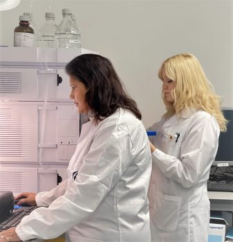 22-12-05_pic_Laura-HPLC Laura Hulkko and Juliane Tania Enas in front of a HPLC